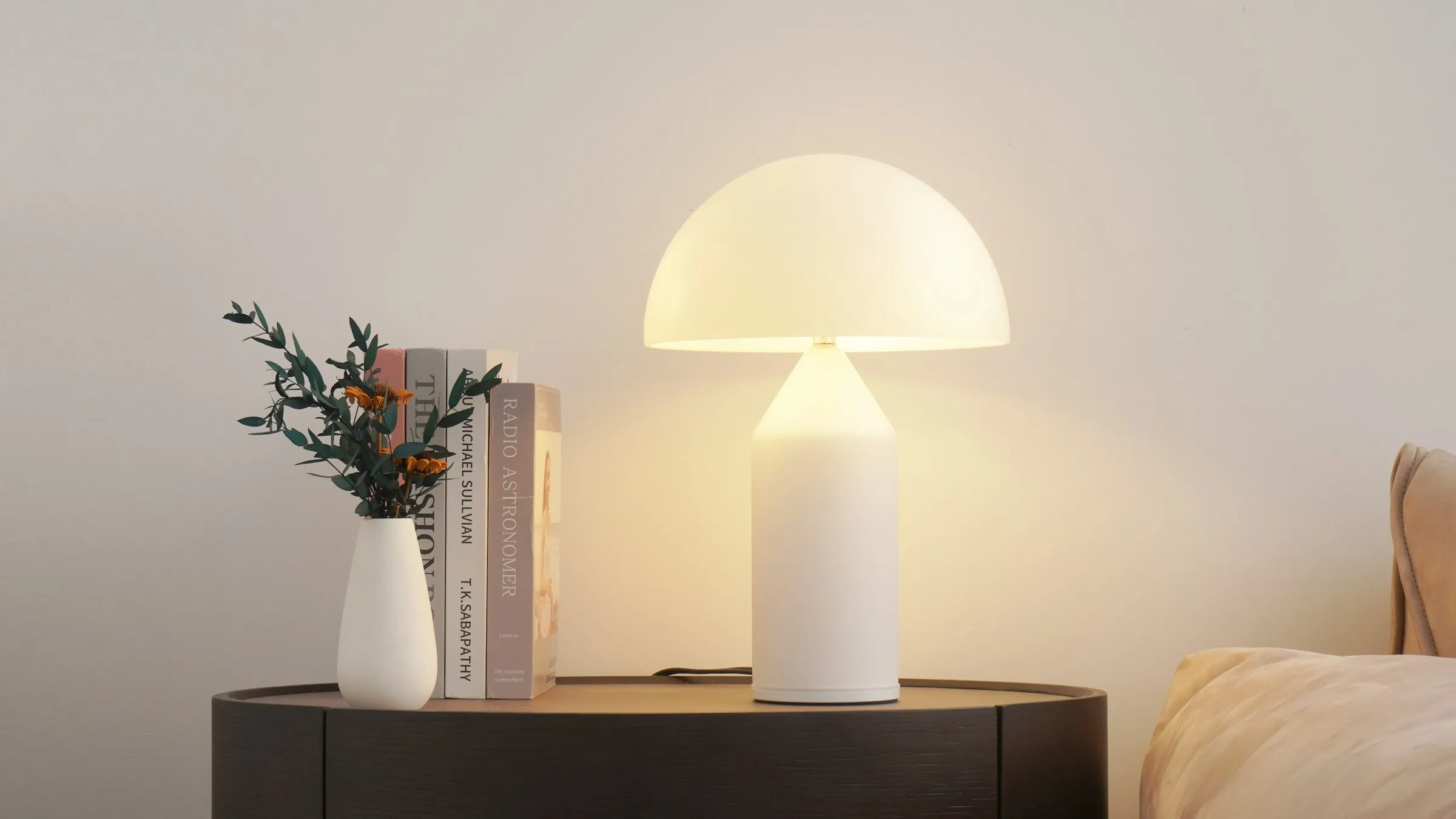 A lit table lamp beside a vase and a stack of books